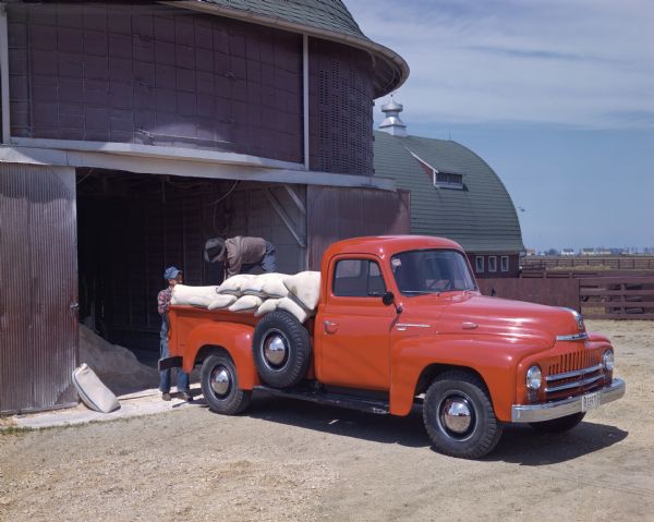 1950 Two men loading bags into a International L-120 truck