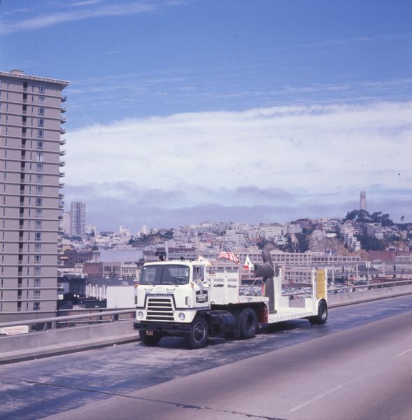 1970 International C-O 4070A Transtar truck hauling the metal statue St. Francis of the Guns on a trailer down a San Francisco highway
