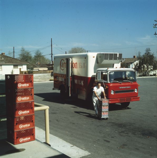 1972 Color photograph of a man unloading cartons of milk from an International truck used by the Carnation Company. The truck appears to be an Internati
