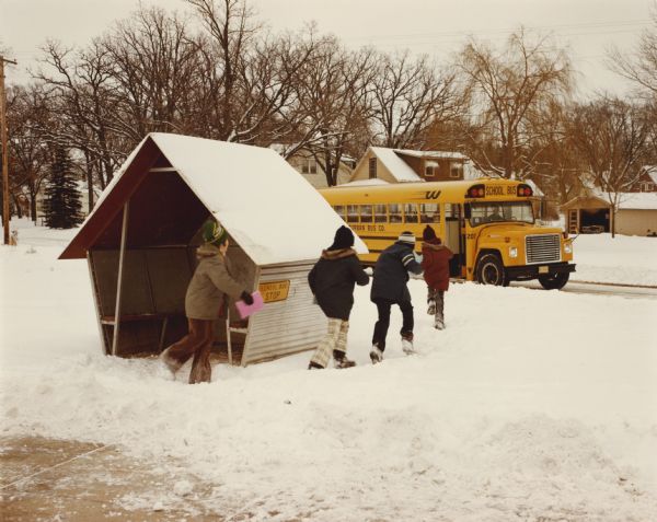 1975 kids walking through snow while leaving a metal bus shelter to board an International school bus